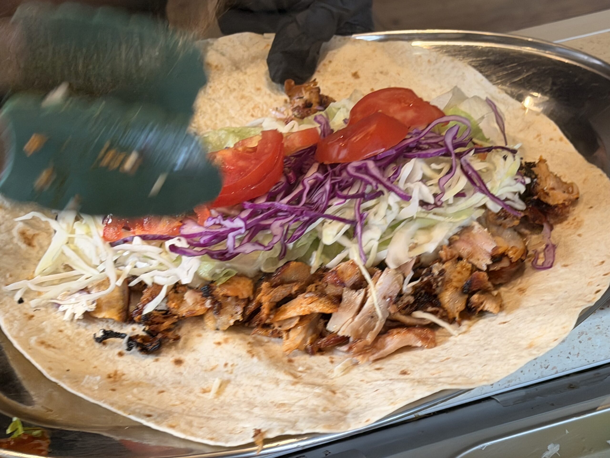 Shawarma wrap with sliced meat, tomato and cabbage being prepared at Que?bab